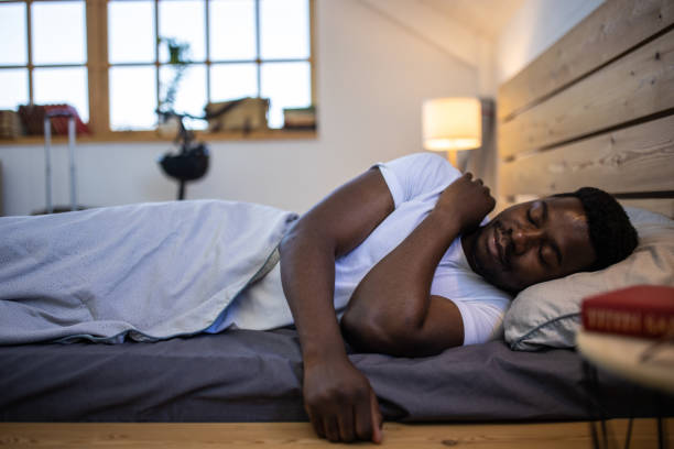 молодой человек спит в постели утром дома - лежать на боку стоковые фото и изображения