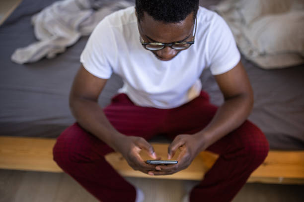 istock Young man in pajamas using smartphone while sitting on bed in the morning in bedroom 1344246587