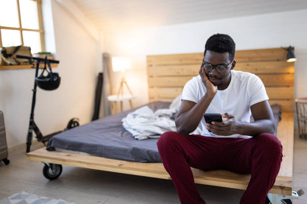 istock Young man in pajamas using smartphone while sitting on bed in the morning in bedroom 1344247340