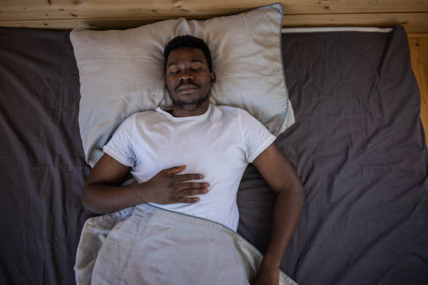 jeune homme dormant dans son lit à la maison - supine photos et images de collection