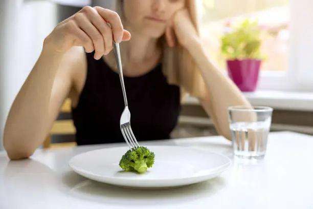 Photo of dieting problems, eating disorder - unhappy woman looking at small broccoli portion on the plate