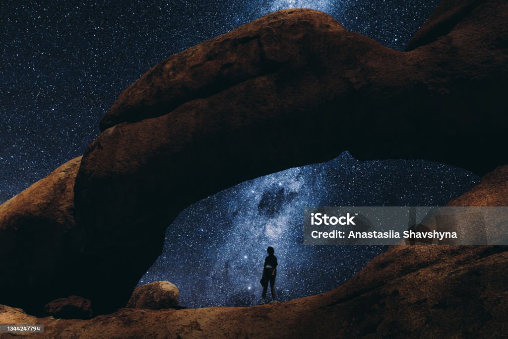 Woman staying inside the natural arch looking at the million of stars in Namibia Silhouette of woman exploring there Spitzkoppe scenic landscape during the night full of stars and Milky Way Night Stock Photo