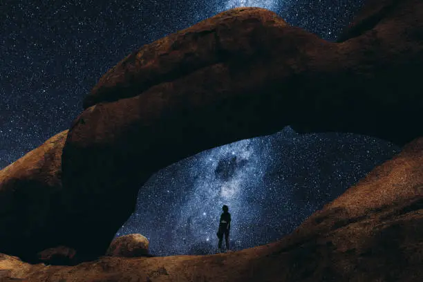 Photo of Woman staying inside the natural arch looking at the million of stars in Namibia