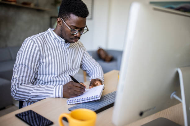 istock Young man writing down important information in notepad while telecommuting from his home office 1344248160