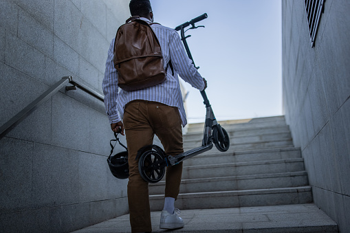 Rear view of young businessman going home after work with push scooter