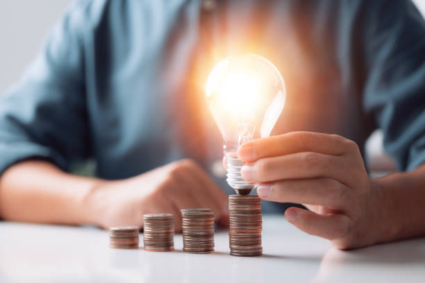 istock Businessman holding and putting lightbulb on coins stack on table for saving energy and money concept 1344249122