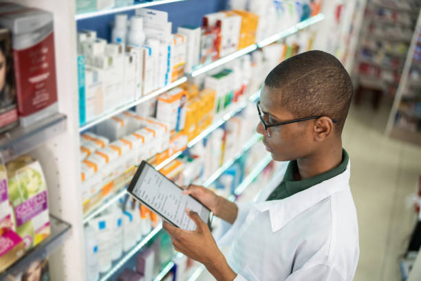 jovem farmacêutico verificando as prateleiras com um tablet digital na farmácia - pharmacy medicine pharmacist storage room - fotografias e filmes do acervo