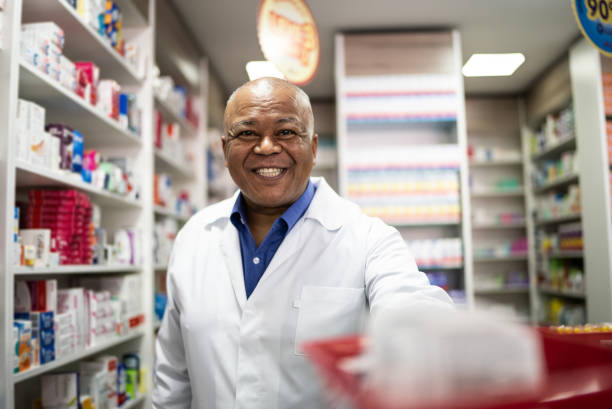 porträt eines leitenden apothekers, der einen korb in der apotheke anbietet - pharmacy pharmacist smiling pill stock-fotos und bilder