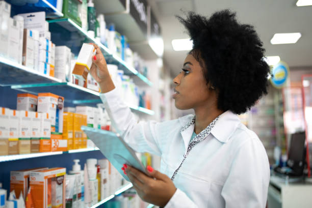 young pharmacist checking the shelves with a digital tablet at the pharmacy - pharmacist pharmacy pill medicine imagens e fotografias de stock