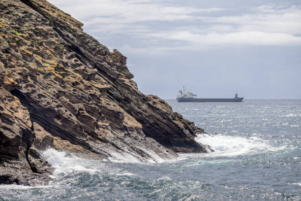 Identifiable small freight ship in front of the rock filled coast outside Ponta Delgada the main city on the Portuguese Azorean Island San Miguel in the center of the North Atlantic Ocean