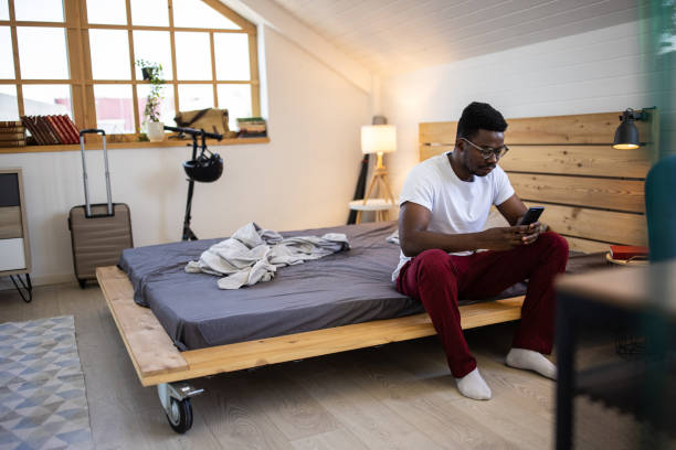 istock Young man surfing the net using smart phone and smiling while sitting on bed in bedroom 1344251805