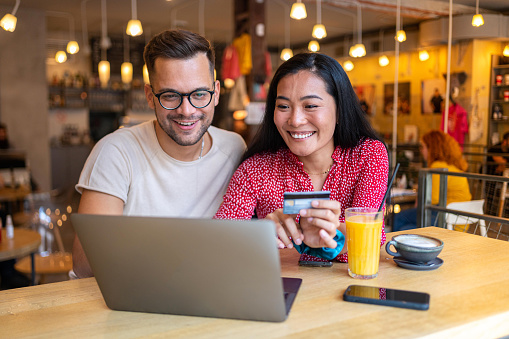 Modern multiracial young couple online shopping together on the laptop, from the modern and cozy coffee shop
