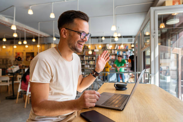 Modern male freelancer having an online meeting via video call, while working from an modern cafeteria