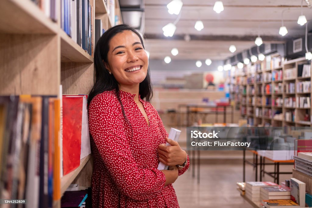 Charming female librarian of Asian ethnicity Portrait of female librarian/bookseller of Asian ethnicity, during her workday in the library/book store Post-Secondary Education Stock Photo