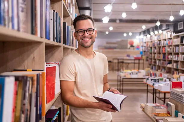 Portrait of a charming male student, at the library/bookstore looking for the right literature/book