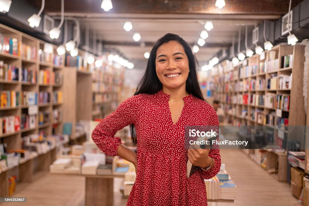 Portrait of modern female librarian of Asian ethnicity Portrait of female librarian/bookseller of Asian ethnicity, during her workday in the library/book store Library Stock Photo