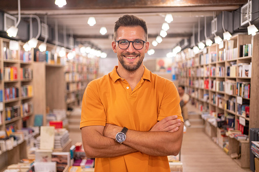 Portrait of  charming male librarian/bookseller, during his workday in the library/book store