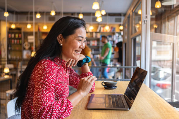 Dedicated female student of Asian ethnicity having online class via laptop from the modern cafeteria A modern young woman of Asian ethnicity, having a video call via laptop, at the modern and cozy cafeteria internet facebook social networking plan stock pictures, royalty-free photos & images