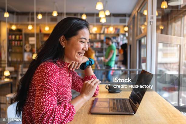 Dedicated Female Student Of Asian Ethnicity Having Online Class Via Laptop From The Modern Cafeteria Stock Photo - Download Image Now