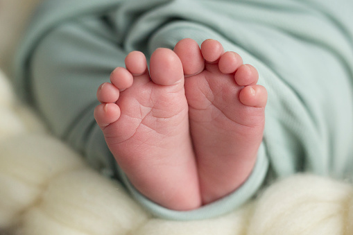 Children's sweet feet wrapped in a turquoise blanket on beige background, close up.