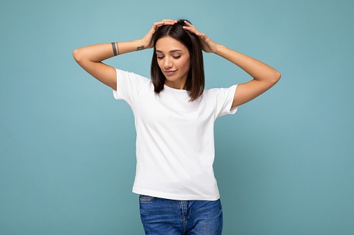 Photo of positive happy sexy young beautiful brunette woman with sincere emotions wearing stylish white t-shirt for mockup isolated over blue background with empty space.