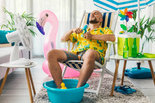 Summer vacations at home and hot weather Man spending summer vacations at home, he is cooling himself with electric fans and sitting on a deckchair covid secure photos stock pictures, royalty-free photos & images