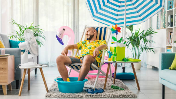 Man having a staycation and resting on a deckchair at home Man relaxing on a deckchair at home in the living room, he is having a staycation and pretending he is on a beach hand fan photos stock pictures, royalty-free photos & images