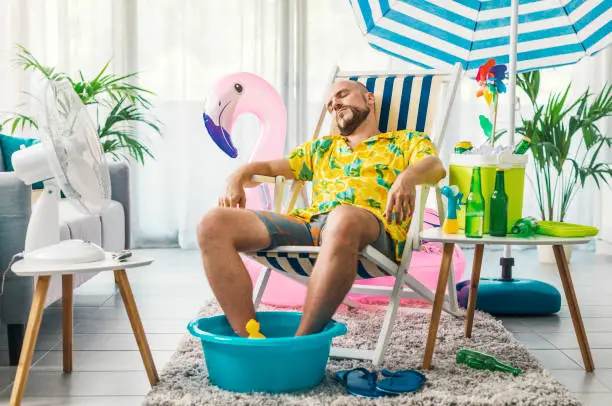 Man relaxing on a deckchair at home in the living room, he is having a staycation and pretending he is on a beach