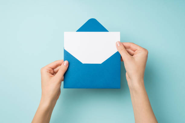 first person top view photo of female hands holding open blue envelope with white paper sheet on isolated pastel blue background with empty space - opening mail letter envelope imagens e fotografias de stock