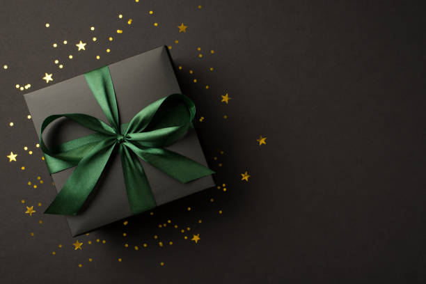 top view photo of stylish giftbox with green ribbon bow golden stars and confetti on isolated black background with copyspace - green friday stockfoto's en -beelden