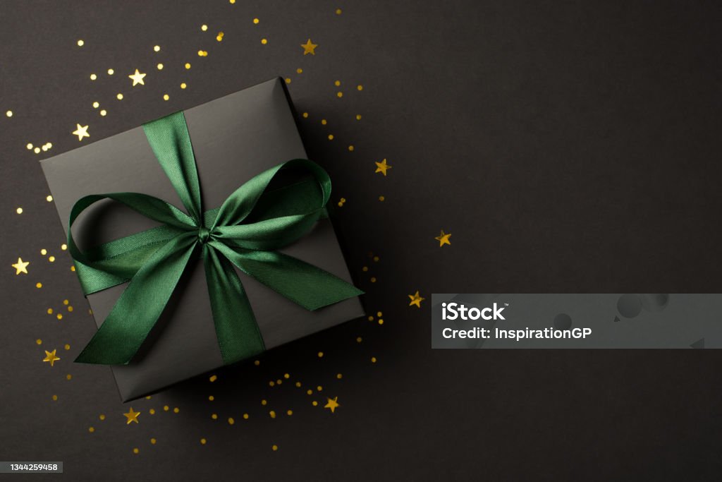 Top view photo of stylish giftbox with green ribbon bow golden stars and confetti on isolated black background with copyspace Gift Stock Photo