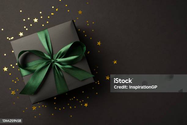 Top View Photo Of Stylish Giftbox With Green Ribbon Bow Golden Stars And Confetti On Isolated Black Background With Copyspace Stock Photo - Download Image Now