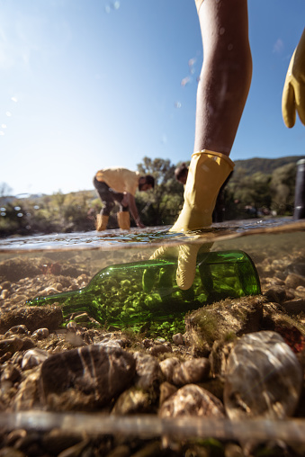 Close-up, human hand picking up glass bottle from river at sunset