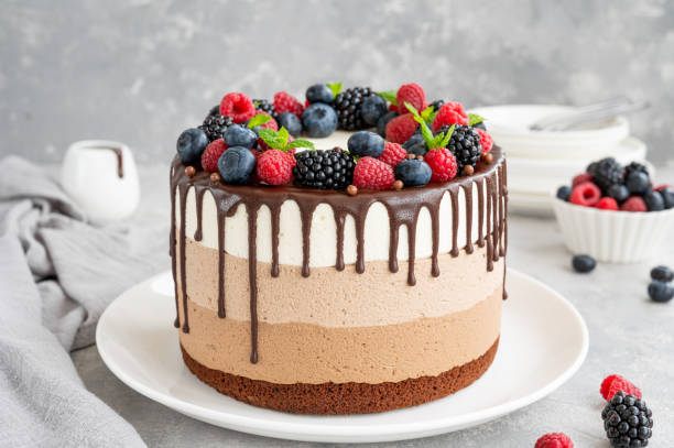 istock Three chocolate mousse cake with chocolate glaze, blueberries, raspberries and blackberries on top on a white plate on a gray concrete background. Cake with three layers of different taste. Copy space. 1344259888