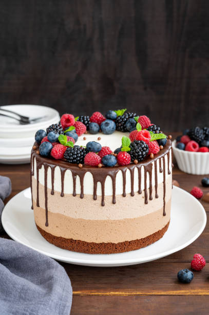 istock Three chocolate mousse cake with chocolate glaze, blueberries, raspberries and blackberries on top on a white plate on a dark wooden background. Cake with three layers of different taste. Copy space. 1344259889