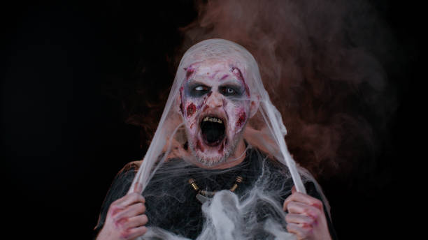istock Scary wounded zombie undead guy making faces, hiding through spider web, smiles terribly, scares 1344261740