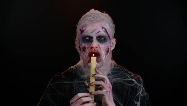 istock Sinister man with horrible scary Halloween zombie makeup making faces, spells conjures over a candle 1344261807