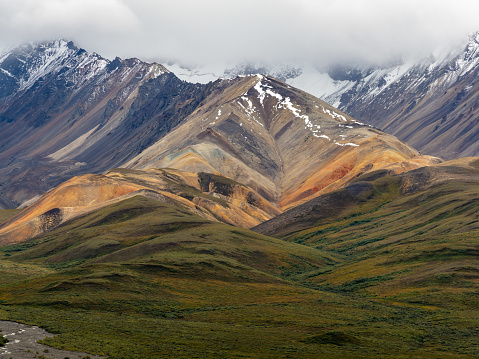 Photo of beautiful Polychrome Pass in Denali National Park in Alaska with dramatic clouds and sky and snow covered peaks. This was taken just days before the park road was forced to be closed due to landslide activity in the area of this pass. The Toklat River runs through.