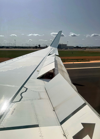 After landing view along the aluminum skinned wing of a modern jet airliner showing full flap and airbrake extension after landing with reverse thrust deployed and aerodynamic control surface details of flaps, ailerons, airbrakes and winglets, looking towards the horizon.