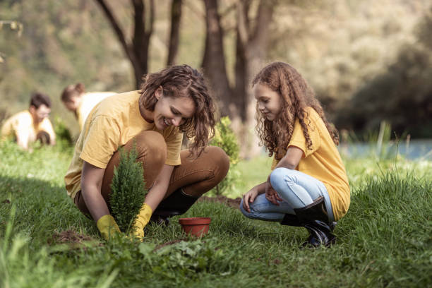 Mother and daughter planting a tree by river stock photo