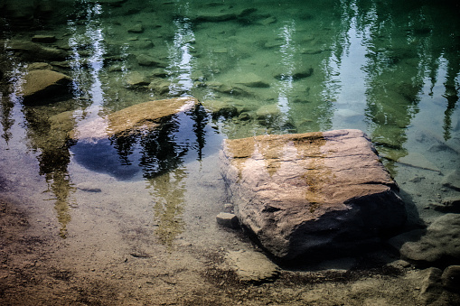 Big stones under water reflecting trees on the surface