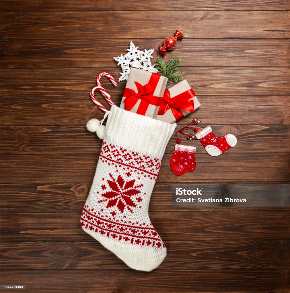 Christmas stocking white with gifts, sweets, snowflake on a wooden background. View from above. Christmas Stocking Stock Photo