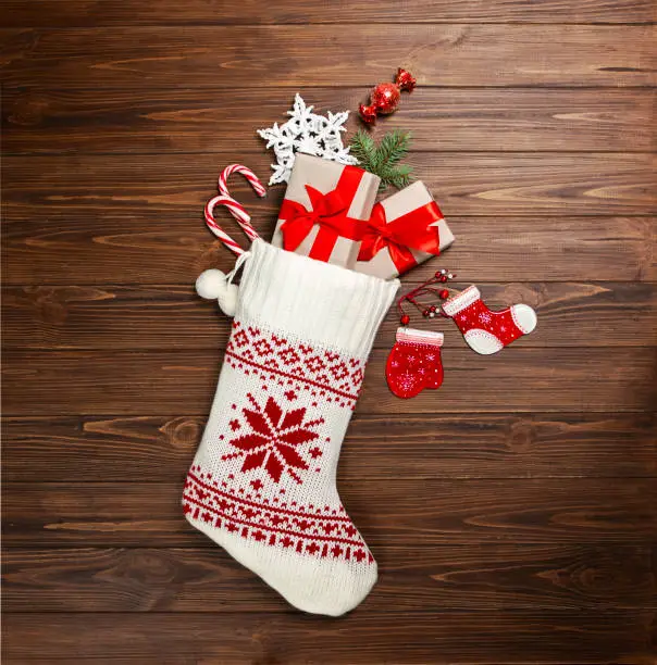 Photo of Christmas stocking white with gifts, sweets, snowflake on a wooden background. View from above.
