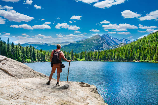 Man standing on the top of the rock looking at beautiful mountains view. Man on summer mountain hiking trip relaxing by the lake. Rocky Mountains National Park, Bear Lake, Colorado, USA.