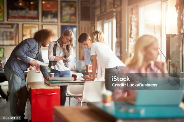 Selective Focus On Group Of Young Adult People Gathered Around The Table Analyzing New Design With Teamleader Stock Photo - Download Image Now