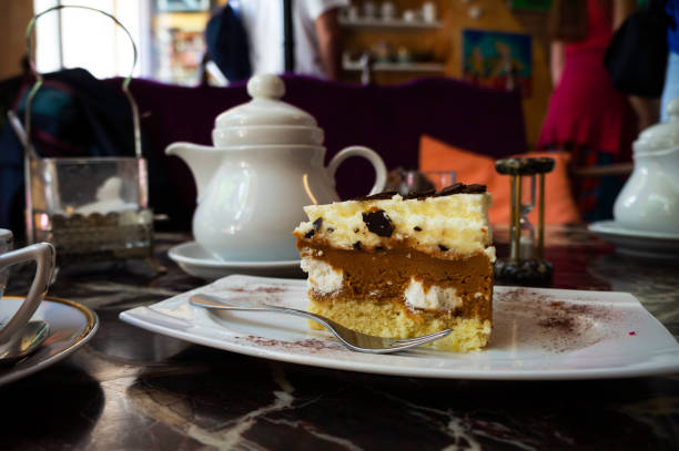 A piece of cake on plate and tea in teapot on a table in tea shop.