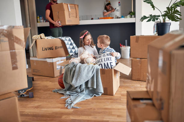 minor caucasian brother and sister, playing in empty cardboard box, happy in new apartment, with their parents in the background minor caucasian brother and sister, playing in empty cardboard box, happy in new apartment, with their parents in the background. new apartment, new begining unpacking stock pictures, royalty-free photos & images