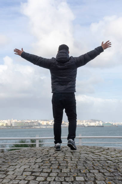 istock Man from the back watching the ocean with his hands up feeling free 1344287642