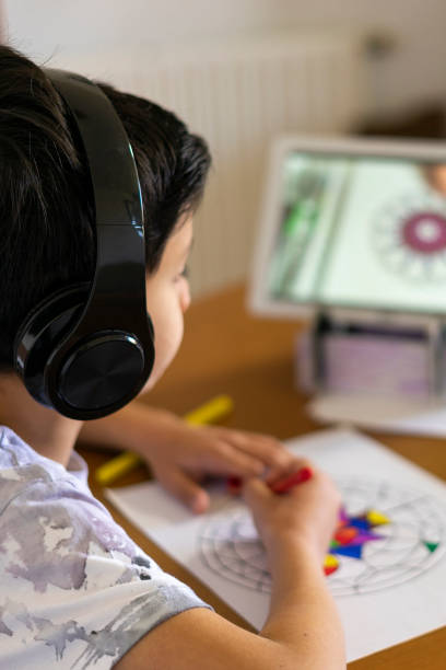 istock Boy painting a mandala with his colored markers watching a tutorial on his tablet with headphones at home 1344289062