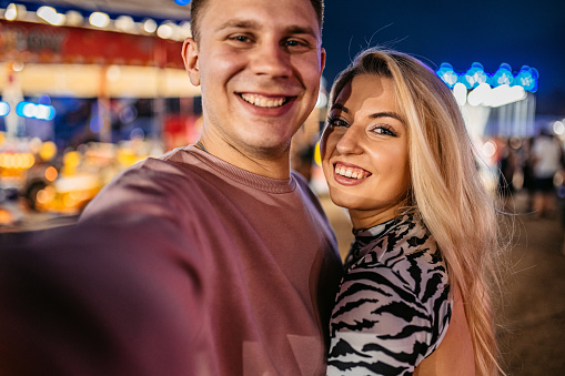 Young Caucasian heterosexual couple making selfie in an amusement park.